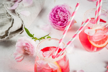 Summer refreshment drinks. Light pink rose cocktail, with rose wine, tea rose petals, lemon. On a white stone concrete table. With striped pink tubules, petals and rose flowers. Copy space