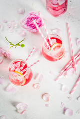 Summer refreshment drinks. Light pink rose cocktail, with rose wine, tea rose petals, lemon. On a white stone concrete table. With striped pink tubules, petals and rose flowers. Copy space