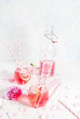 Summer refreshment drinks. Light pink rose cocktail, with rose wine, tea rose petals, lemon. On a white stone concrete table. With striped pink tubules, petals and rose flowers. Copy space