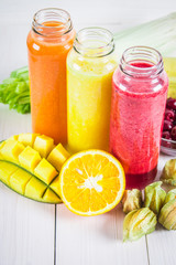 Multicolored smoothies in bottles of mango, orange, banana, celery, berries, on a wooden table.
