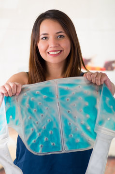 Close up of a beautiful smiling woman holding an ice gel pack with both hands, medical concept, in office background