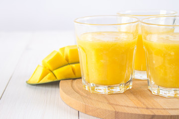 Yellow smoothie of mango, banana and orange on a white wooden table.