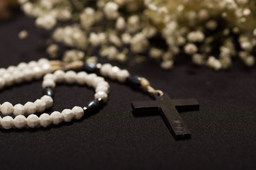 Close up of a rosary beads with blurred white small flowers, black background
