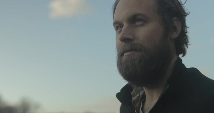 A confident bearded man stands outside