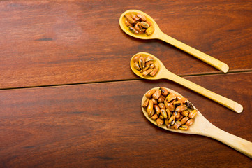 Wooden spoons with toasted corn grains, known as tostado in south america, spread around bowl containing yellow salsa, seen from above