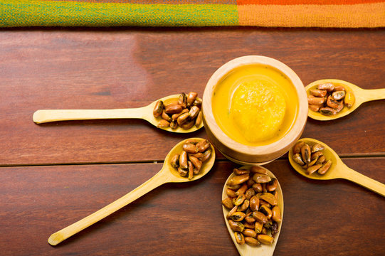 Wooden spoons with toasted corn grains, known as tostado in south america, spread around bowl containing yellow salsa, seen from above