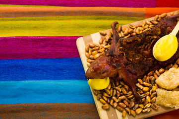 Traditional ecuadorian dish, grilled guinea pig spread out onto wooden board, tostados, bacon skin and lemons on the side, seen from above