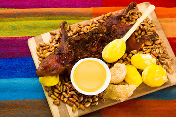 Traditional ecuadorian dish, grilled guinea pig spread out onto wooden board, tostados, bacon skin...