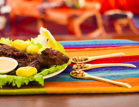 Traditional ecuadorian dish, grilled guinea pig spread out onto green plate, potatoes, tostados and lemons on the side, seen from above