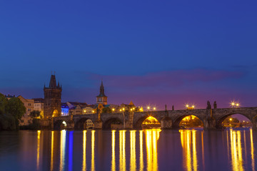 Charles bridge and riverbank with reflections in Prague, Czech republic during sunrise blue hour