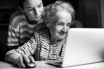 Girl teaches an elderly woman working on a laptop. Black-and-white photo.