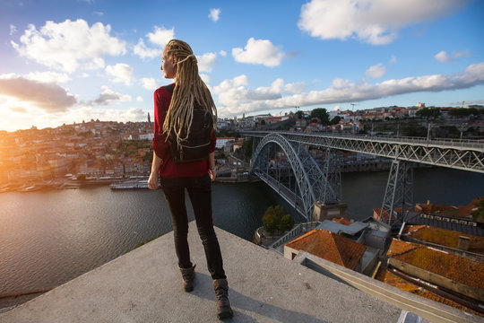 Young beautiful woman with blond dreadlocks meets sunset on the viewing platform opposite the Dom Luis I bridge across the Douro river in Porto, Portugal.