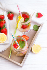 Mineral  water with fresh strawberries, lemon  and mint in jar on a white wooden background, copy space