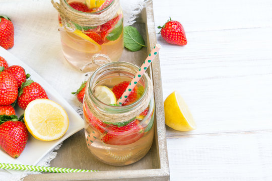 Mineral  water with fresh strawberries, lemon  and mint in jar on a white wooden background, copy space