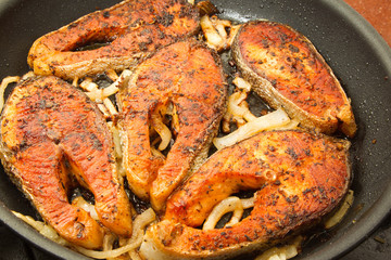 Pieces of trout fried in a frying pan with onions