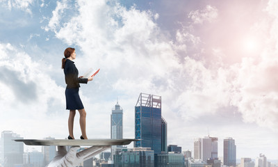 Attractive businesswoman on metal tray with red book in hands against cityscape background