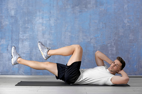 Handsome man doing bicycle crunch on color wall background