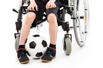 Disabled child boy sitting on wheelchair holding soccer ball
