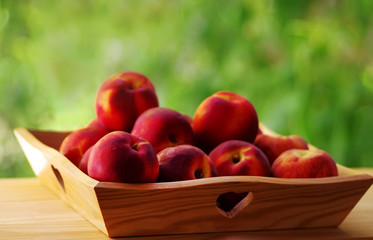 Fresh juicy peaches in wooden basket on green background