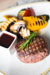 Close-up of pork steak with garnish, grilled vegetables, champignon mushrooms, pepper, zucchini, with sauce, decorated with rosemary, beautiful trendy serve, healthy tasty food, restaurant
