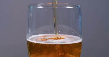 Pouring lager beer on a pint glass with neutral background, slow motion