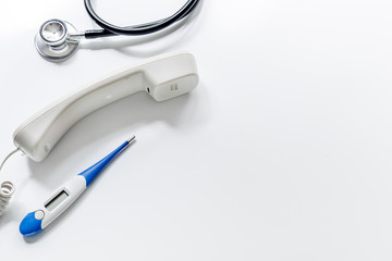 Phone handset, phonendoscope and thermometer on isolated white background top view call doctor space for text