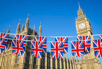 Fototapeta na wymiar Two rows of Union Jack bunting flying in front of the Houses of Parliament at Westminster Palace with Big Ben under bright blue sky in London, England