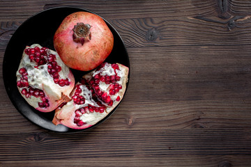 Red sliced pomegranate on plate on wooden background top view mock up