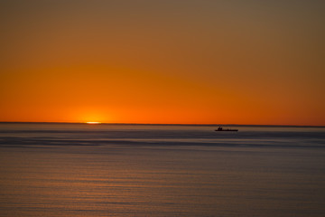 A minimalistic shot of a cargo ship on the horizon of the ocean at sunset