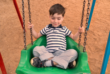 A happy boy is riding on a swing