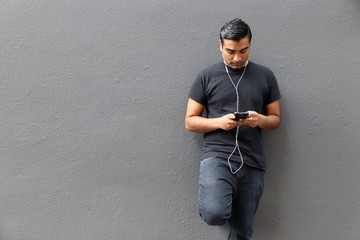 Handsome man wearing black shirt standing against gray wall looking down at phone