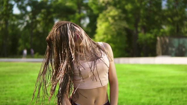 Young beautiful girl with dreads dancing in a park. Beautiful woman listening to music and dancing during a sunny day. Slowmotion shot.