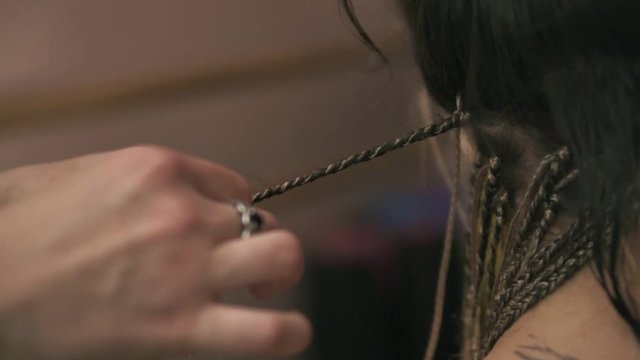 Closeup view of the hairdresser's hands doing dreads for a young woman in the hair salon. Slowmotion shot
