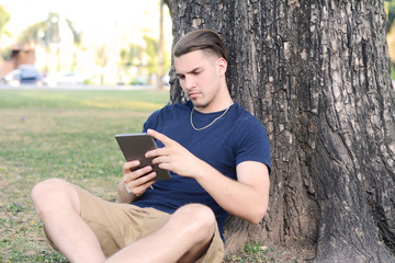 Obraz premium Young man using tablet with headphones in park.