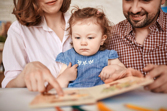 Portrait of young parents reading story to cute little girl and showing pictures