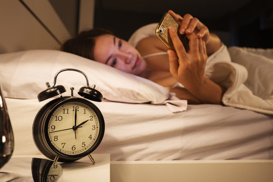 clock show 2 O'clock and woman using her smartphone on bed in the bedroom