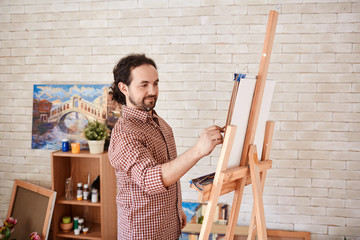 Portrait of talented inspired artist enjoying painting picture in art studio, smiling