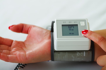 Close up of a young patient using an automatic tensiometer in her arm, in a doctor consulting room background