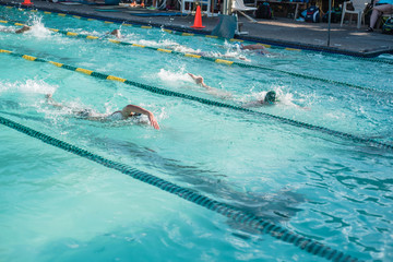 Close-up action shot of teen boy swimming front crawl stroke style in the blue water outdoor race pool. Focus on arm and water splash, some motion blurs. Summer, swimming race and competition concept.