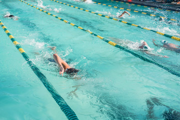 Close-up action shot of teen boy swimming front crawl stroke style in the blue water outdoor race pool. Focus on arm and water splash, some motion blurs. Summer, swimming race and competition concept.
