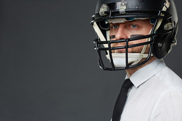 Closeup portrait of confident middle aged businessman with army paint on his face wearing helmet and looking at camera away against grey background