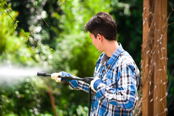 Handsome young man wearing square pattern blue holding high pressure water gun, on a garden background