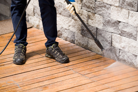 Close up of a man cleaning terrace with a power washer - high water pressure cleaner on wooden terrace surface