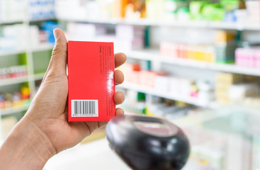 Pharmacist scanning price on a red medicine box with barcode reader in pharmacy store