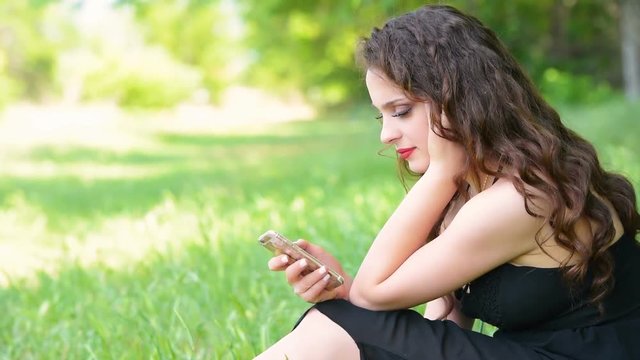Beautiful young woman sitting on grass using smartphone camera tilt