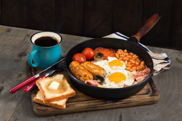 English breakfast with sausages, bacon, fried eggs, beans, toast, coffee