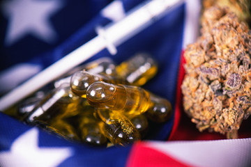 Detail of cannabis CBD oil capsules and bud in front of american flag