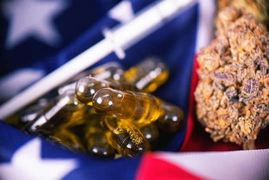 Detail of cannabis CBD oil capsules and bud in front of american flag