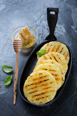 Grilled pineapple slices with addition of honey in a black cast-iron frying pan, studio shot