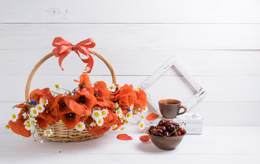 Daisy and poppies bouquet in basket with cup tea, sweet cherry and photo frame